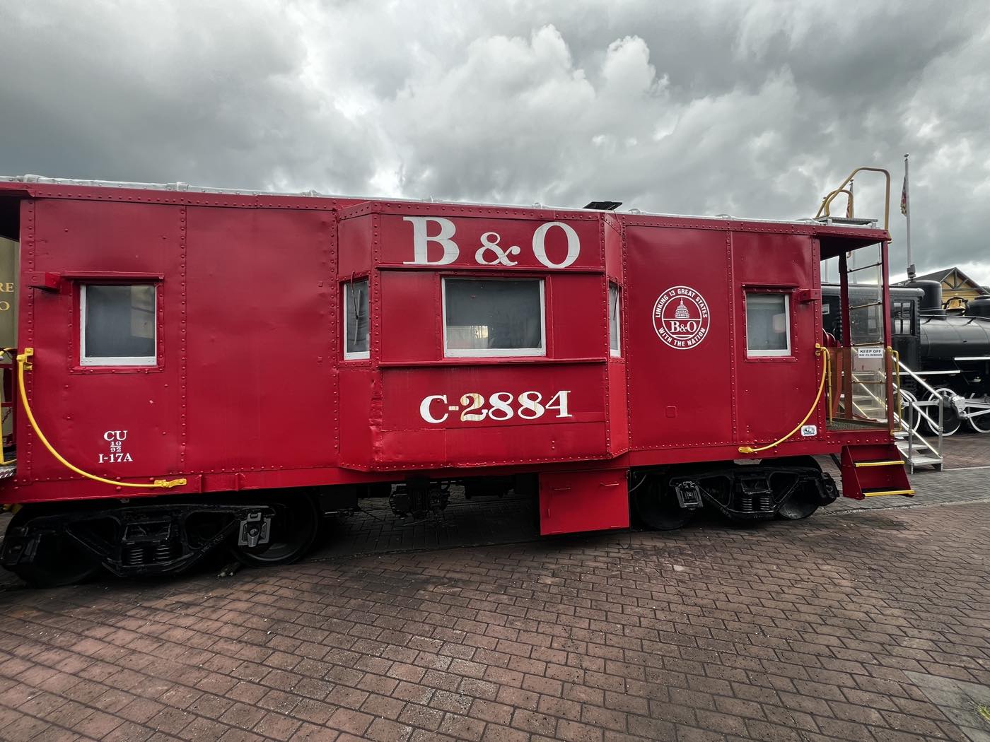 A bright red Baltimore and Ohio caboose lettered B&O C-2884, with white window frames and a yellow handrail, on brick paving.
