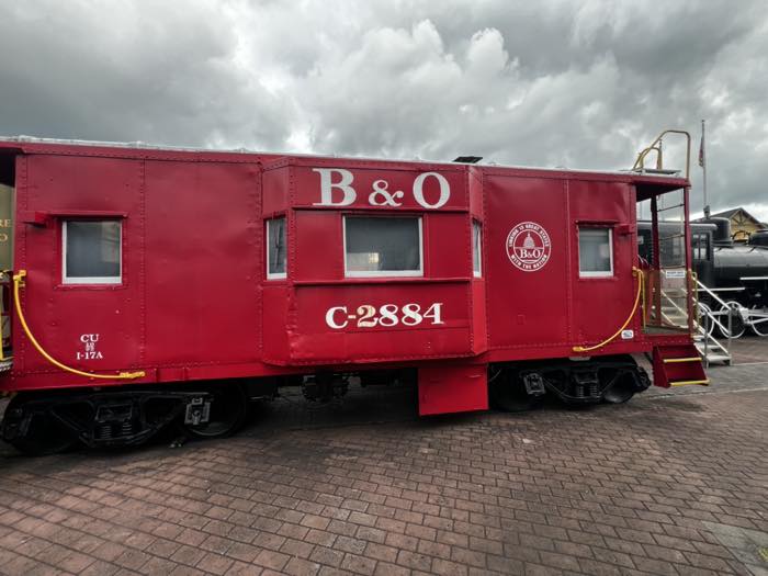 A bright red Baltimore and Ohio caboose lettered B&O C-2884, with white window frames and a yellow handrail, on brick paving.